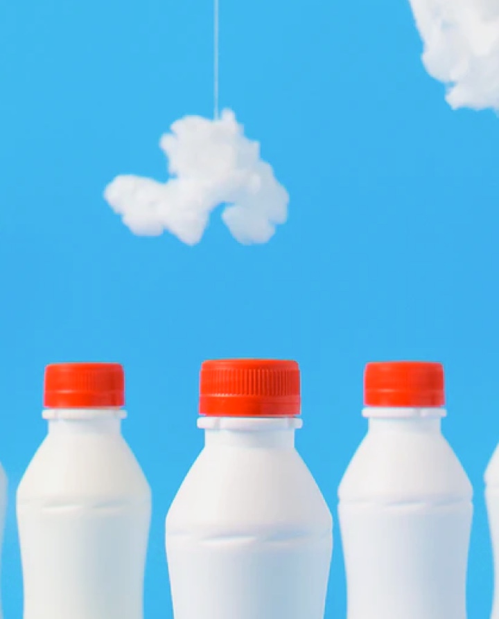 4 bouteilles de lait au bouchon rouge devant un ciel peu nuageux