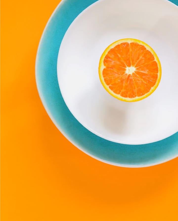 bol bleu de lait sur un support orange vif et une tranche d'orange sur le lait
