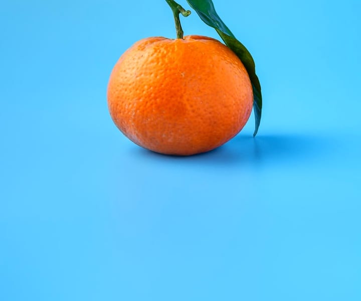 une clémentine avec sa feuille posée sur un fond bleu ciel
