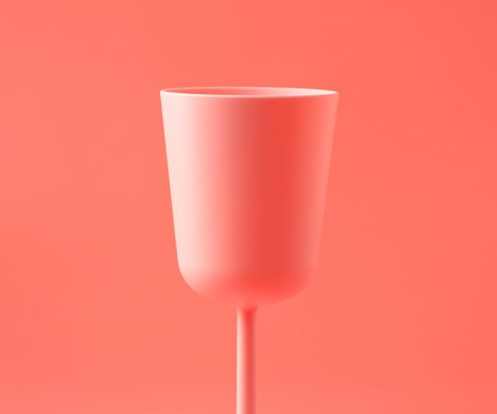 un verre à pied rose saumon posé devant un fond de même couleur